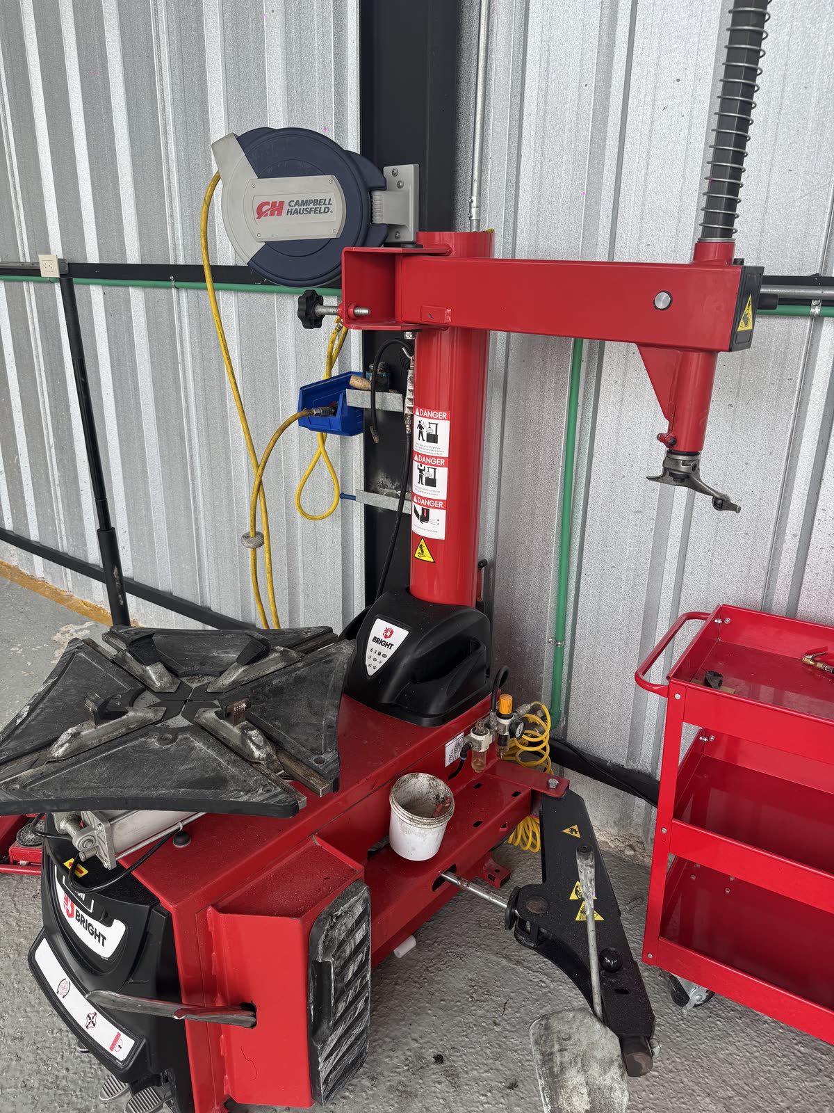 Desmontadora automática de gomas, roja, junto a un carrito de herramientas